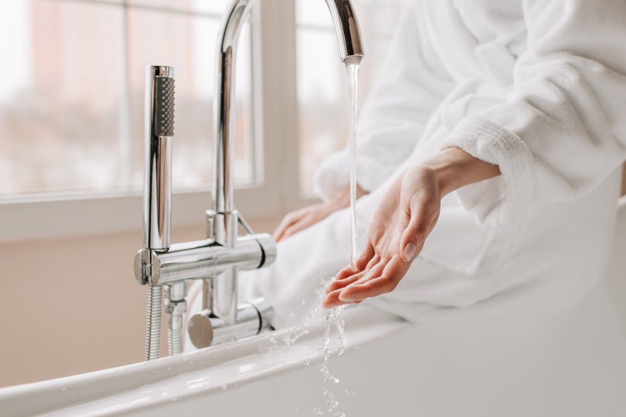 Close-up of a person in a bathrobe feeling the flowing water in a bathtub.