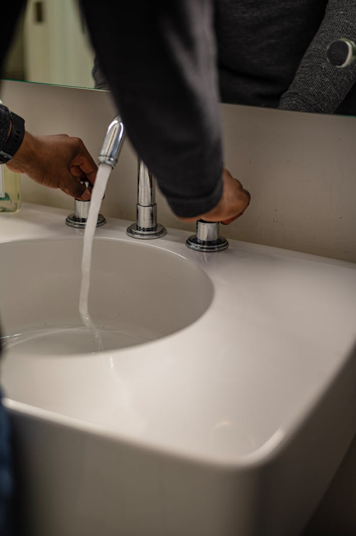 Close-up of hands adjusting water flow in a modern ceramic sink with stainless faucet.