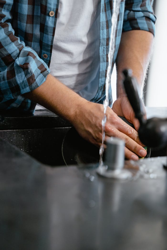 Adult washing dishes with running water in a modern kitchen setting.